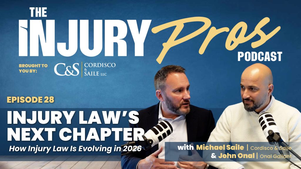 Two men sit at a table speaking during an episode of "The Injury Pros Podcast" discussing the future of injury law, with show branding and episode details in the background.